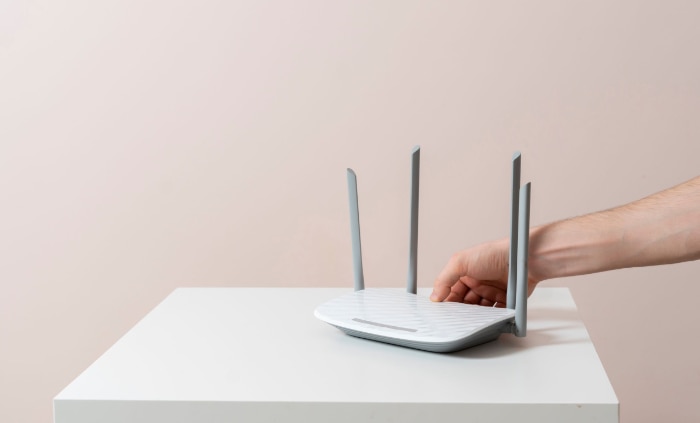 Hand adjusting a white wireless router on a minimalist table