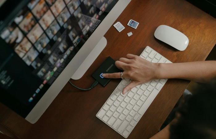 Hand connecting external SSD to computer with memory cards nearby