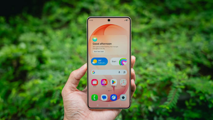 Hand holding Samsung Galaxy phone with green background