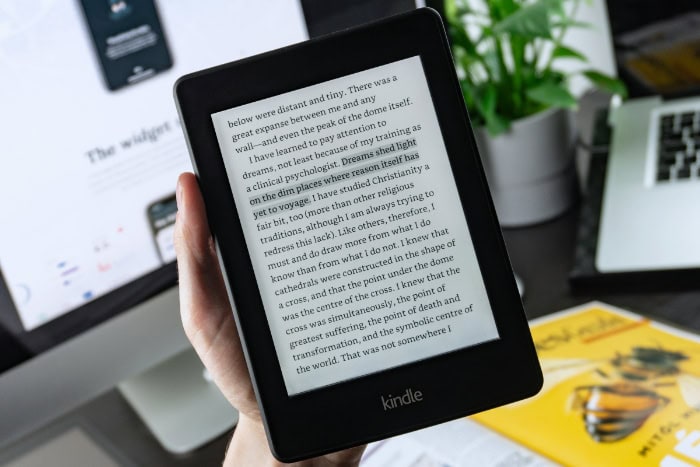 Hand holding a Kindle indoors near a desk