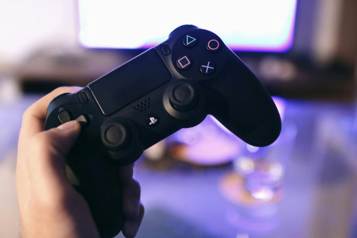 Hand holding a PlayStation controller in front of a screen