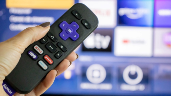 Hand holding a Roku remote with streaming interface