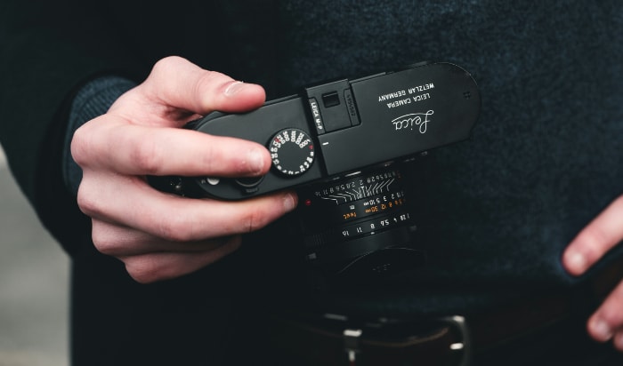 Hand holding a black Leica M7 camera with visible settings dial