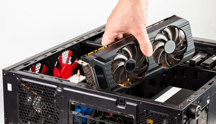 Hand holding a dual fan black graphics card above an open PC case