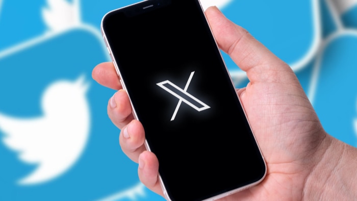 Hand holding a smartphone displaying the Twitter X logo