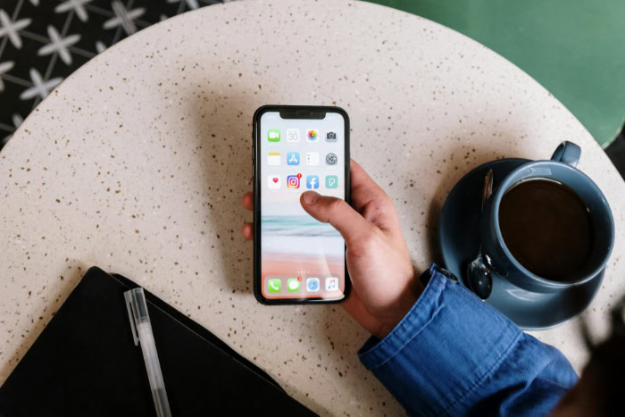 Hand holding a smartphone on a table with coffee