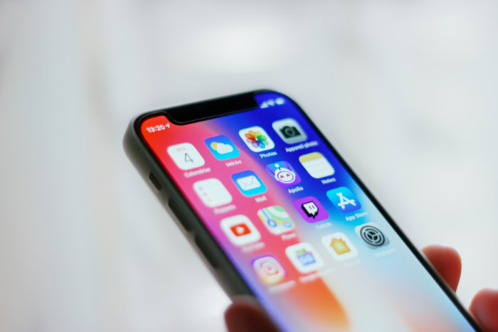 Hand holding iPhone displaying home screen apps