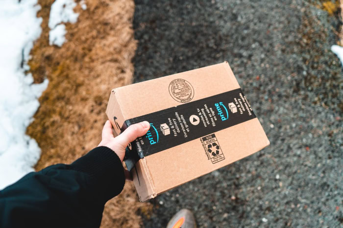 Hand holding small Amazon Prime cardboard box outdoors resized