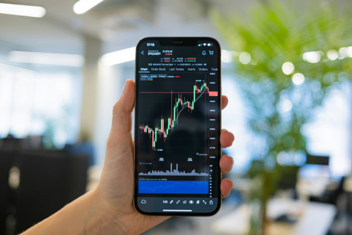 Hand holding smartphone displaying cryptocurrency trading chart