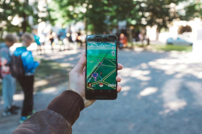 Hand holding smartphone playing Pokemon Go in park