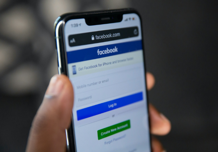 Hand holding smartphone showing Facebook mobile login page