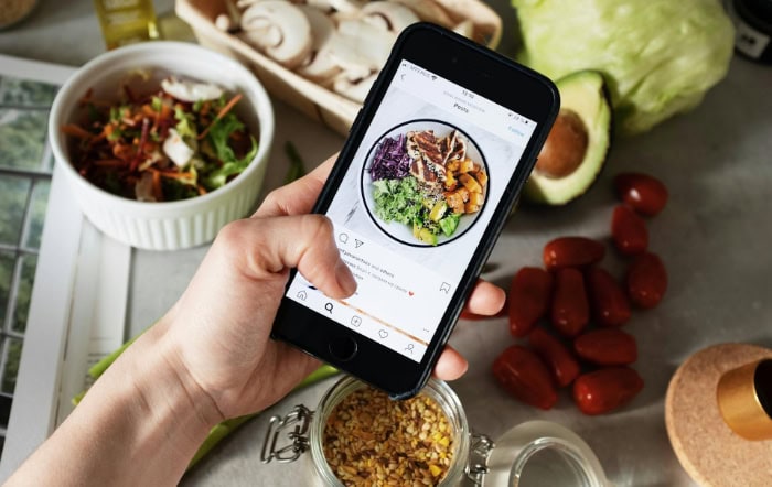 Hand holding smartphone showing Instagram post of colorful salad bowl