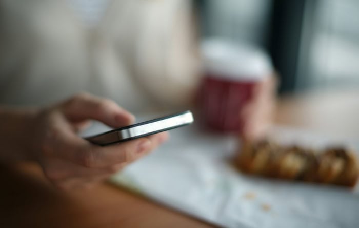 Hand holding smartphone with blurred coffee cup