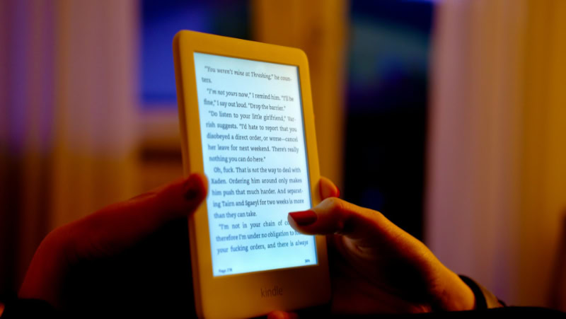 Hand holding white Amazon Kindle e reader in dark