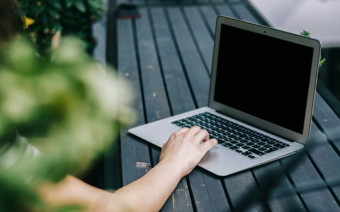 Hand on MacBook touchpad outdoors with plants