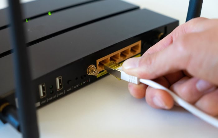 Hand plugging Ethernet cable into black router with multiple ports