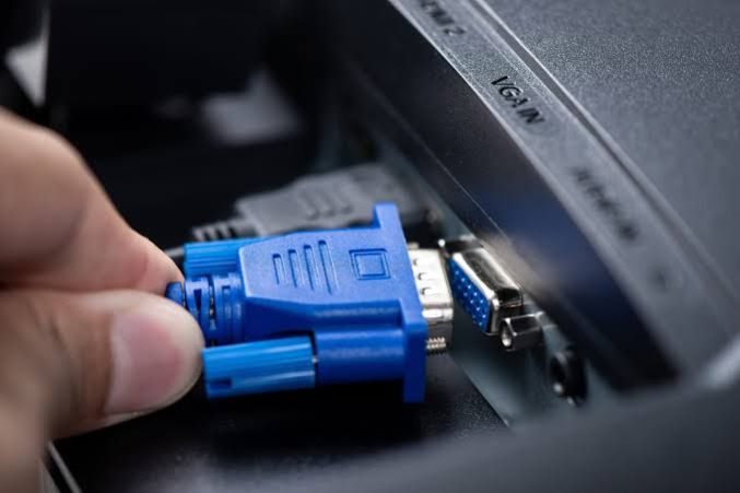 Hand plugging blue VGA cable into monitor port
