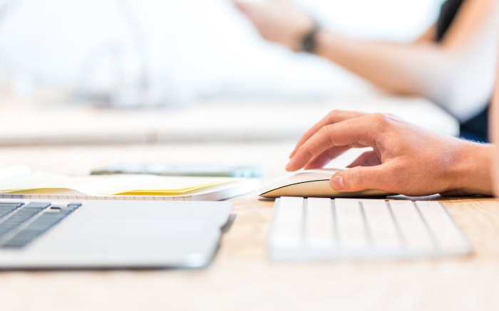 Hand using computer mouse on desk with keyboard visible