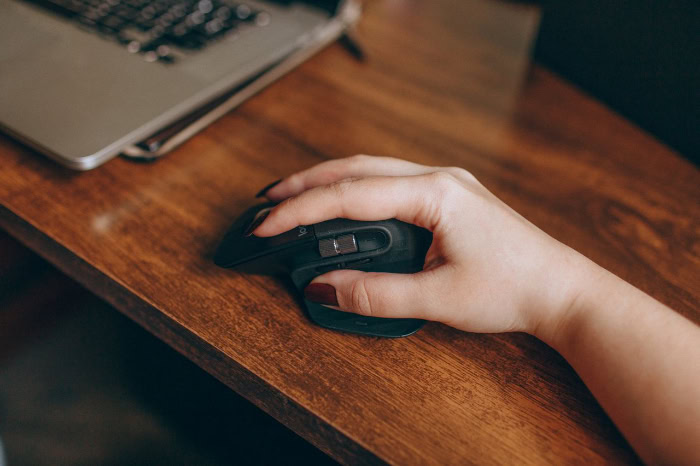 Hand using ergonomic wireless computer mouse on wooden desk