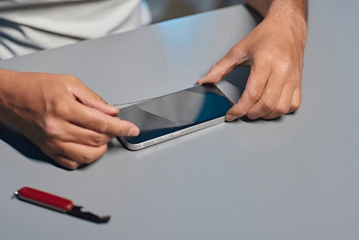 Hands applying screen protector to smartphone on gray surface