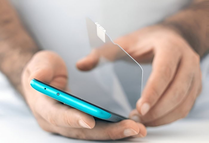 Hands applying transparent screen protector to blue smartphone