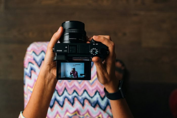 Hands holding a Sony Alpha camera with LCD screen active