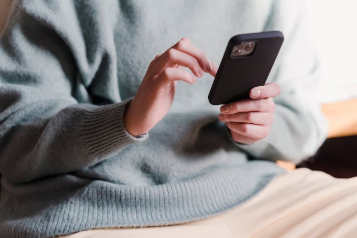 Hands holding black smartphone in grey sweater