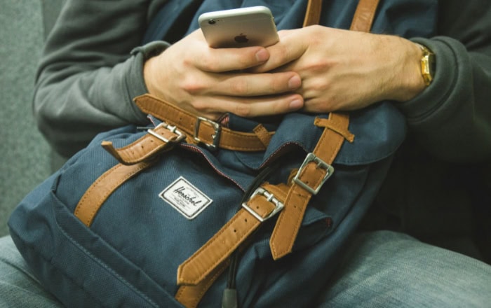 Hands holding iPhone over Herschel backpack