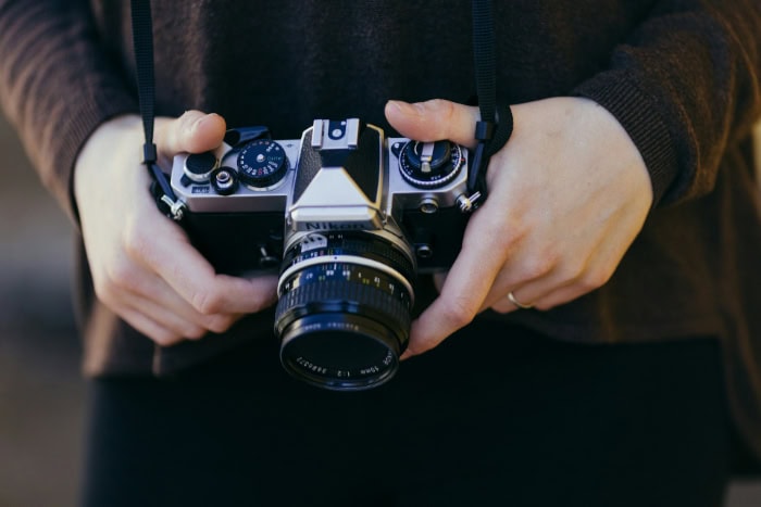 Hands holding vintage Nikon film camera with manual controls