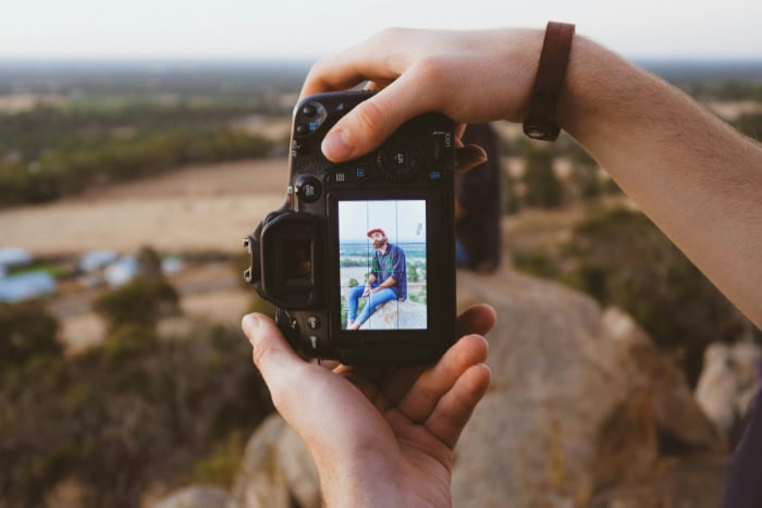 Hands photographing a person outdoors using a DSLR camera