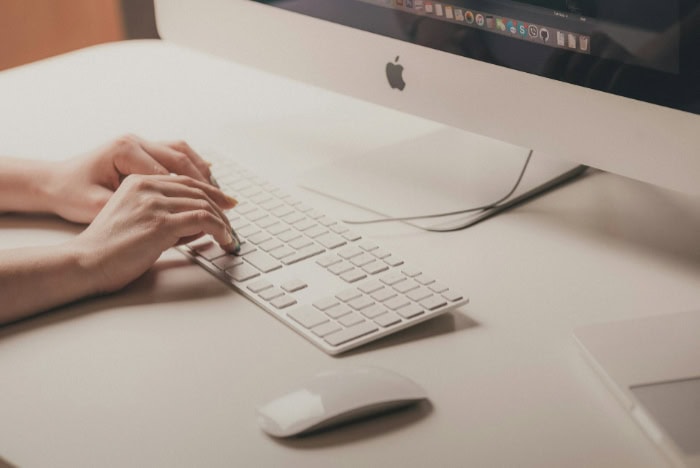 Hands typing on Apple keyboard with iMac display