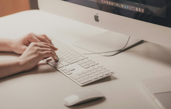 Hands typing on Apple keyboard with iMac in background