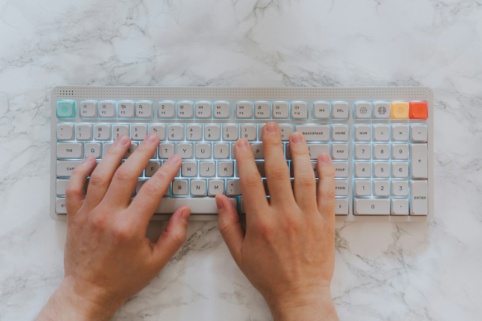 Hands typing on a backlit mechanical keyboard on marble