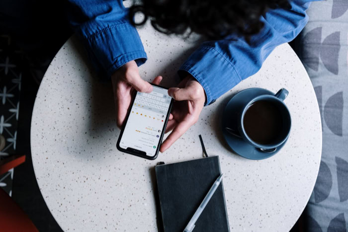 Hands typing on a smartphone beside coffee and a notebook