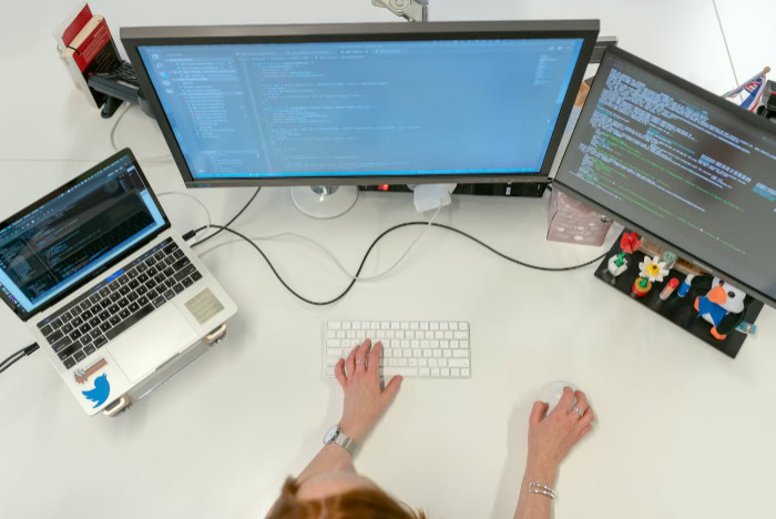 Hands typing on keyboard with triple monitor coding setup