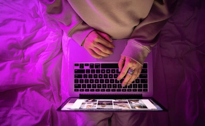 Hands typing on laptop keyboard with purple lighting