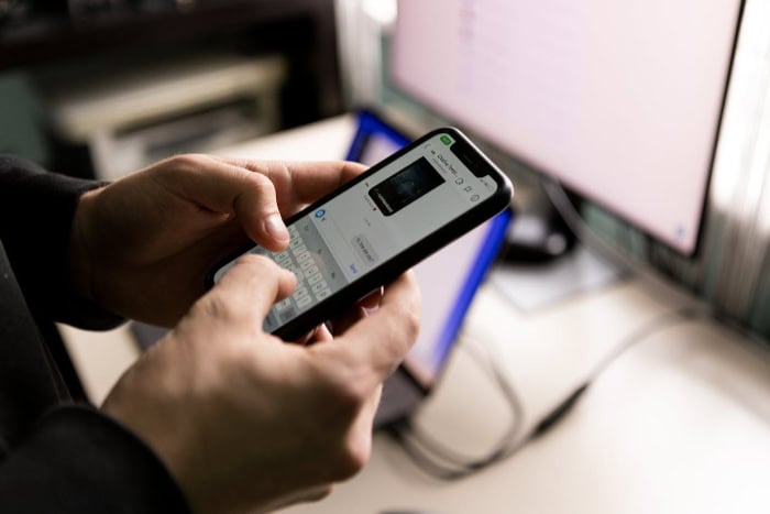 Hands typing on smartphone with laptop screen in background