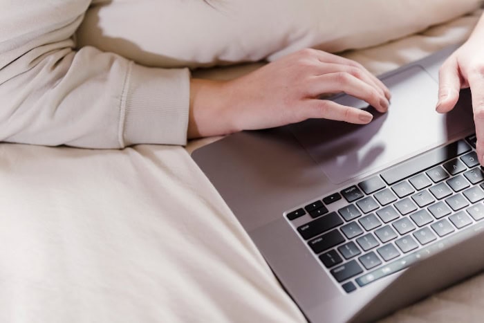 Hands using a laptop while lying on a bed