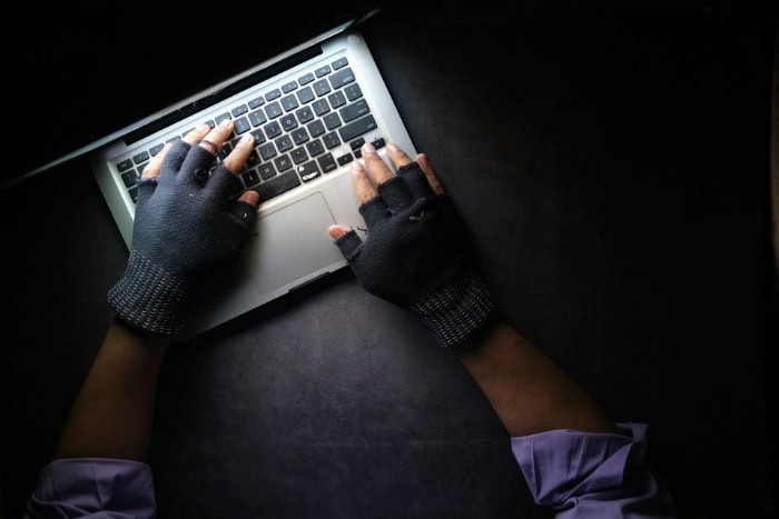 Hands wearing black gloves typing on laptop keyboard