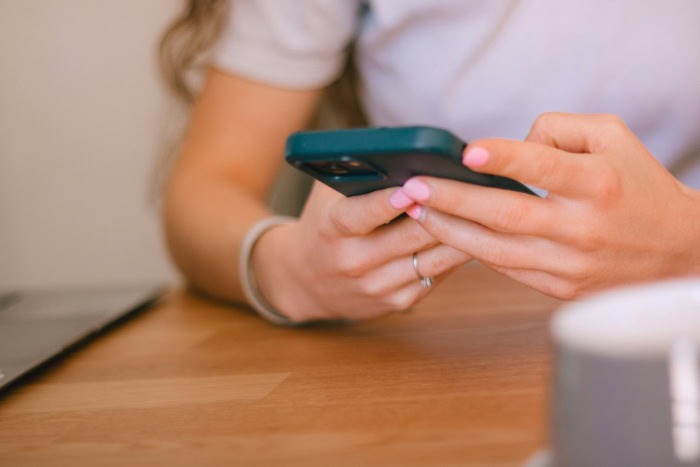 Hands with pink nails using a smartphone on table