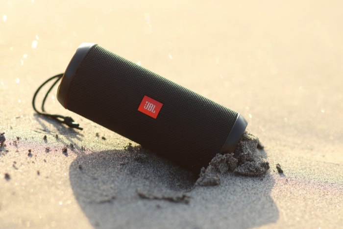 JBL portable Bluetooth speaker resting on sand