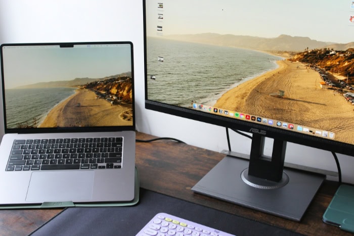 Laptop and monitor displaying coastal scene on wooden desk