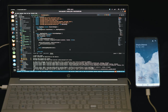 Laptop coding with smartphone weather app