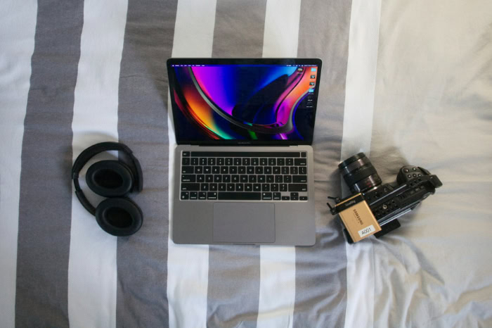 Laptop headphones and professional camera on a bed