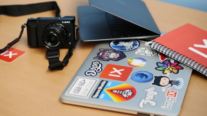 Laptop with colorful stickers next to camera and notebook