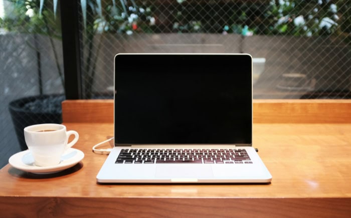 MacBook with black screen on wooden table next to coffee cup