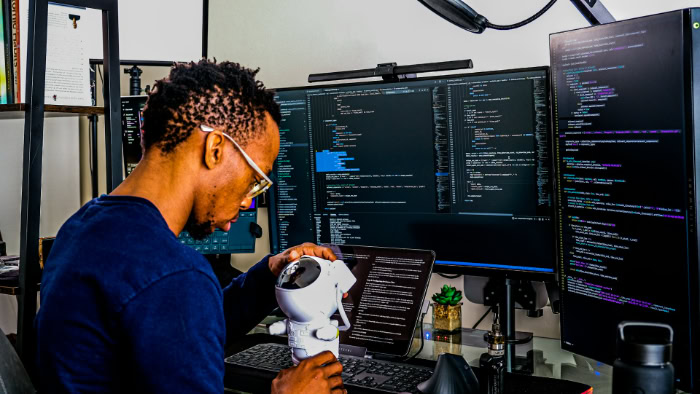 Male software developer coding at multi screen desk setup
