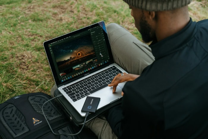 Man editing photos on a laptop outdoors with external SSD