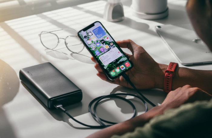 Man using a smartphone connected to a power bank on a desk