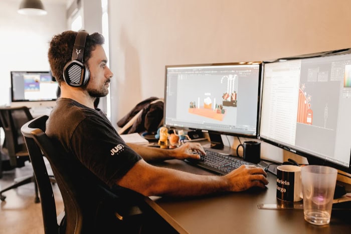 Man using dual monitors for 3D design wearing headphones